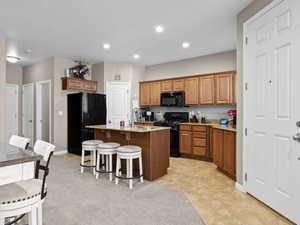 Kitchen with a kitchen island with sink, black appliances, light stone countertops, sink, and a kitchen breakfast bar