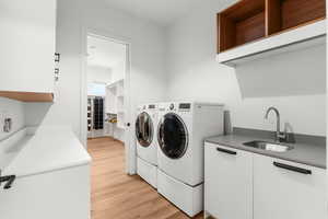 Washroom with light wood finished floors, cabinet space, a sink, and washer and dryer