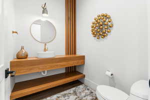 Half bath featuring a sink, baseboards, wood finished floors, and toilet