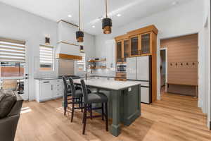 Kitchen featuring freestanding refrigerator, glass insert cabinets, white cabinetry, decorative light fixtures, and stainless steel microwave