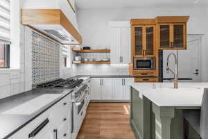 Kitchen featuring tasteful backsplash, stainless steel appliances, white cabinets, open shelves, and glass insert cabinets