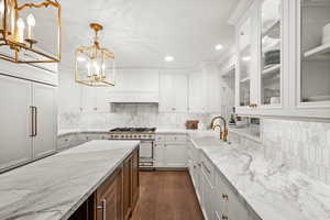 Kitchen with backsplash, light stone counters, white range, white cabinets, and hanging light fixtures