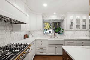 Kitchen featuring light stone counters, white cabinets, stainless steel gas range, sink, and custom exhaust hood