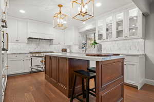 Kitchen with white cabinetry, a center island, decorative light fixtures, high end range, and dark wood-type flooring