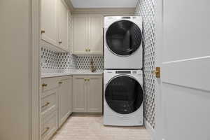 Washroom featuring stacked washer and dryer and cabinets