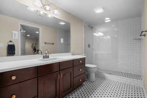 Bathroom featuring tile patterned floors, toilet, vanity, and tiled shower