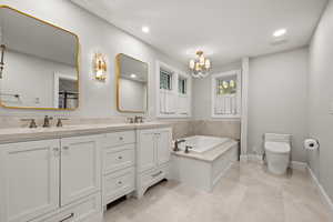 Bathroom with a notable chandelier, vanity, toilet, and a tub to relax in