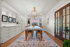 Dining room with a notable chandelier, light hardwood / wood-style floors, french doors, and ornamental molding