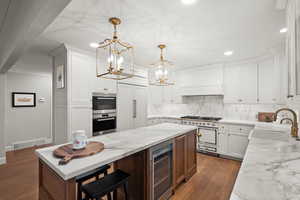 Kitchen with sink, white cabinetry, decorative light fixtures, wine cooler, and premium appliances