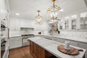 Kitchen with decorative light fixtures, sink, light stone counters, white cabinets, and white stove