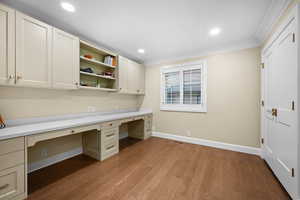 Unfurnished office featuring crown molding, built in desk, and light hardwood / wood-style flooring