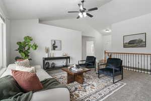 Living room featuring vaulted ceiling, ceiling fan, and carpet flooring