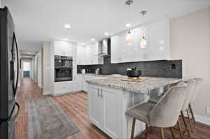 Kitchen with wall chimney range hood, hanging light fixtures, black appliances, and white cabinets