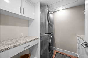 Laundry area featuring hardwood / wood-style floors, stacked washer / dryer, and cabinets