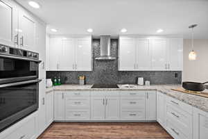 Kitchen featuring white cabinetry, stainless steel double oven, wall chimney exhaust hood, and black electric stovetop