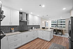 Kitchen with pendant lighting, wall chimney range hood, black appliances, kitchen peninsula, and white cabinets