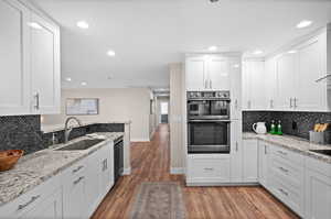 Kitchen featuring double oven, sink, dishwasher, dark hardwood / wood-style floors, and white cabinets