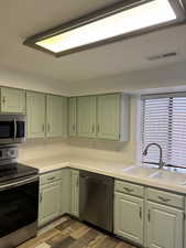 Kitchen with stainless steel appliances, green cabinetry, tile counters, and sink