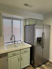 Kitchen featuring sink, stainless steel appliances, green cabinetry, hardwood / wood-style flooring, and tile counters