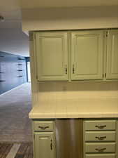 Kitchen with tile counters, dark carpet, and green cabinetry