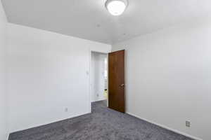 Spare room with dark carpet and baseboards