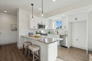 Kitchen with white cabinetry, hanging light fixtures, stainless steel appliances, and light stone countertops