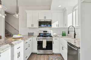 Kitchen with appliances with stainless steel finishes, pendant lighting, sink, white cabinets, and light stone counters