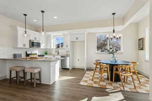 Kitchen with appliances with stainless steel finishes, pendant lighting, white cabinets, kitchen peninsula, and light stone countertops