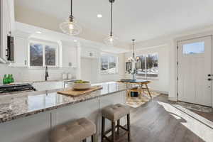 Kitchen with hanging light fixtures, white cabinetry, sink, and light stone counters