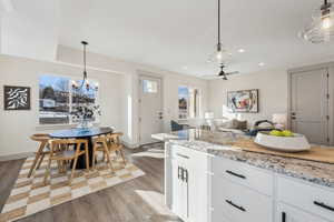 Kitchen with hanging light fixtures, white cabinetry, light stone counters, and light hardwood / wood-style flooring