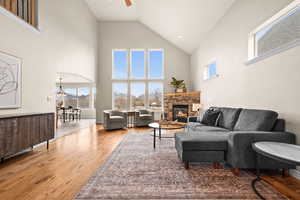 Living room featuring ceiling fan, a stone fireplace, high vaulted ceiling, and wood-type flooring