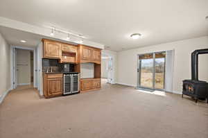 Kitchen with light colored carpet, tasteful backsplash, a wood stove, and beverage cooler