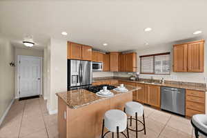 Kitchen featuring appliances with stainless steel finishes, light tile patterned flooring, light stone countertops, and a center island