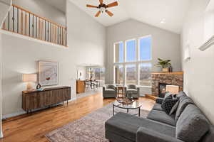 Living room with light hardwood / wood-style floors, high vaulted ceiling, ceiling fan, and a stone fireplace