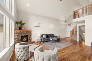 Living room with high vaulted ceiling, a stone fireplace, and hardwood / wood-style floors