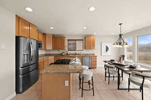 Kitchen with light tile patterned floors, a kitchen island, decorative light fixtures, stainless steel appliances, and light stone countertops