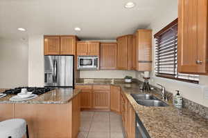 Kitchen featuring sink, light stone countertops, stainless steel appliances, and light tile patterned floors