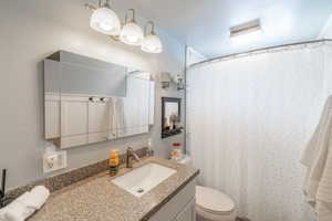 Full bathroom featuring a textured wall, vanity, toilet, and a shower with curtain