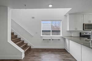 Kitchen featuring dark wood-type flooring, stainless steel appliances, white cabinetry, and dark stone countertops