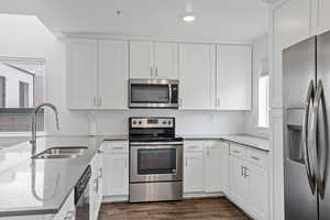 Kitchen with appliances with stainless steel finishes, sink, white cabinetry, and light stone countertops