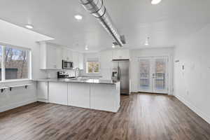 Kitchen with dark hardwood / wood-style flooring, white cabinets, stainless steel appliances, and kitchen peninsula