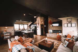 Living room with dark wood-style floors, ceiling fan, a stone fireplace, and recessed lighting.