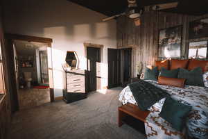 Carpeted primary bedroom with wood walls, ceiling fan, visible vents, and high vaulted ceiling