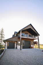 View of front of house with gravel driveway, a balcony, and a large garage.