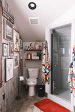 Primary suite bathroom featuring visible vents, toilet, wood finished floors, vaulted ceiling, and a walk in shower.