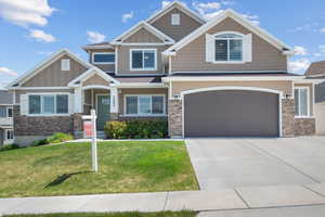 Craftsman-style home featuring board and batten siding, a front yard, a garage, concrete driveway, and stone siding