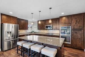 Kitchen featuring appliances with stainless steel finishes, a kitchen island, dark hardwood / wood-style floors, hanging light fixtures, and light stone countertops