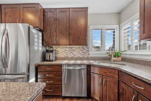 Kitchen featuring dark wood-type flooring, sink, tasteful backsplash, stone counters, and appliances with stainless steel finishes