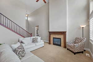Living room with ceiling fan, a fireplace, carpet floors, and a towering ceiling