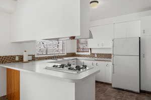 Kitchen featuring white cabinetry, kitchen peninsula, sink, white appliances, and tasteful backsplash